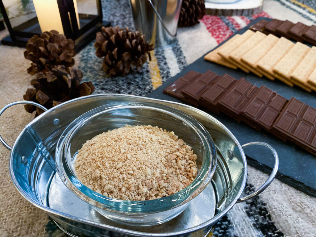 Crushed graham cracker crumbs accompany this boozy chocolate fondue. It's a great s'mores dip recipe and a campfire party idea. It not only tastes fantastic, it looks cure in this galvanized pail on top of a plaid tablecloth and pinecone, with are great camping themed party decorations and camping themed party ideas. They also work great for a campfire party and are easy campfire party ideas. You could also use this as a campfire birthday party ideas.