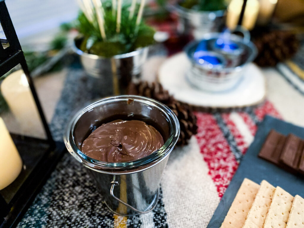 This boozy chocolate fondue is a great s'mores dip recipe and a campfire party idea. It not only tastes fantastic, it looks cure in this galvanized pail on top of a plaid tablecloth and pinecone, with are great camping themed party decorations and camping themed party ideas. They also work great for a campfire party and are easy campfire party ideas. You could also use this as a campfire birthday party ideas.