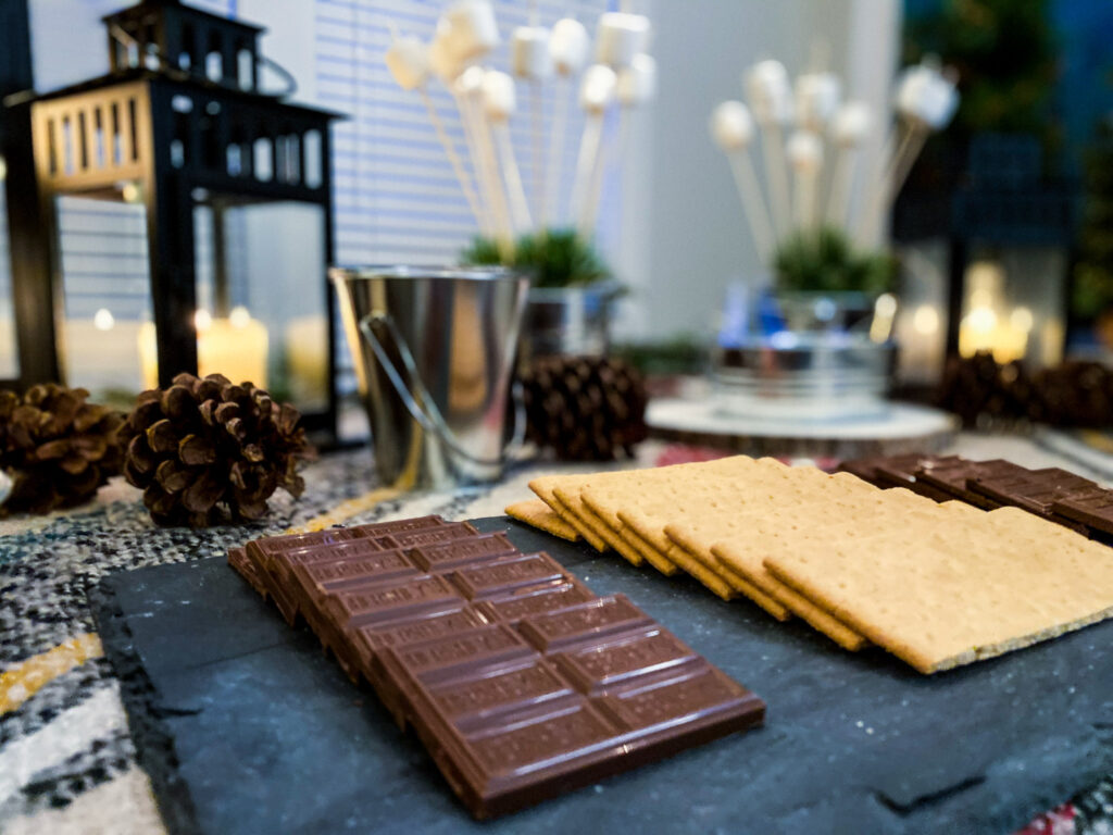 A s'mores bar station is perfect for National S'mores Day, August 10. It contains the classic s'mores ingredients such as Hershey's chocolate bars and graham crackers, as well as marshmallows on a stick.