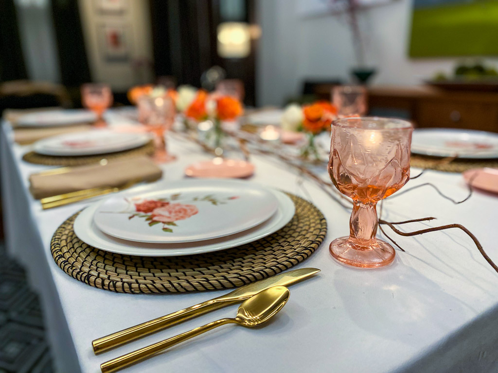 A tablescape with a pink vintage colored glassware set, a seagrass placemat, gold flatware, and vintage melamine plates.