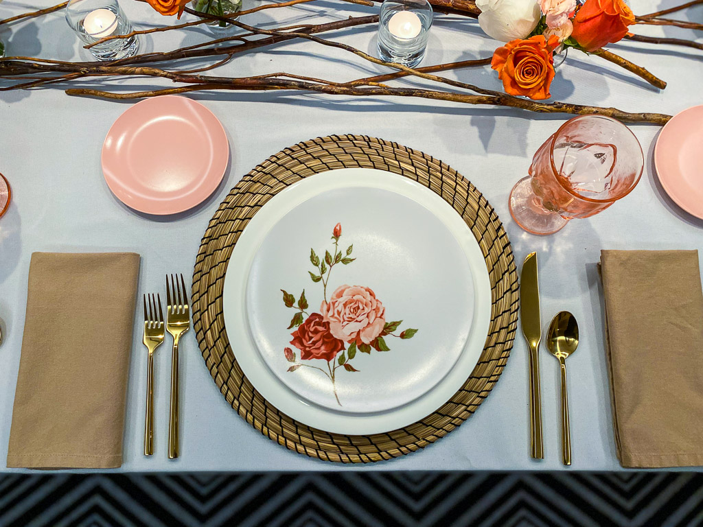 A tablescape with pink vintage colored glassware, a seagrass placemat, gold flatware, and vintage melamine plates.