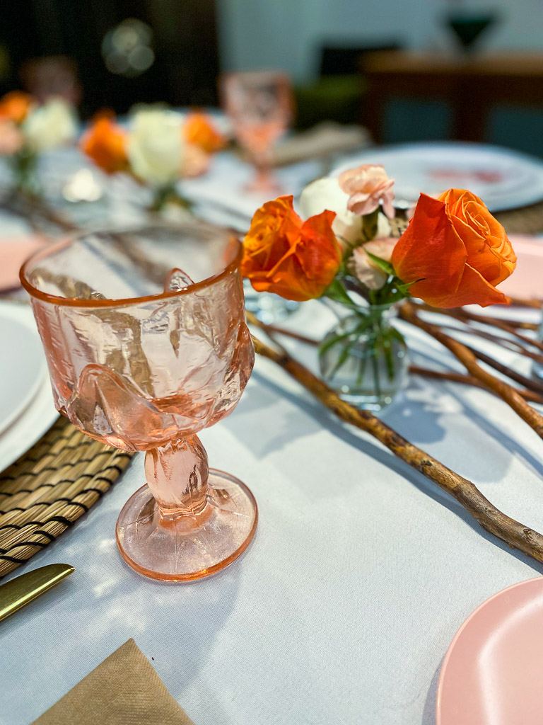 Beautiful pink colored glassware is perfect on this tabletop with a coral colored flower arrangement and vintage plates.