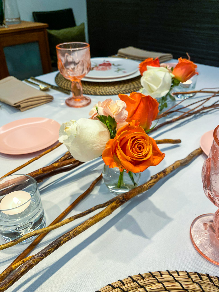 Coral roses in a small bud vase, surrounded by wooden twigs is the perfect complement to the vintage colored glassware on the tabletop.