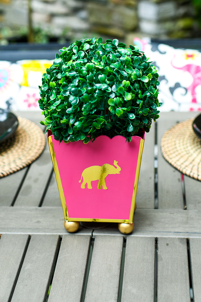 A pink cachepot with shiny gold trim and topped with a green boxwood ball is one of our easy outdoor table decoration ideas.