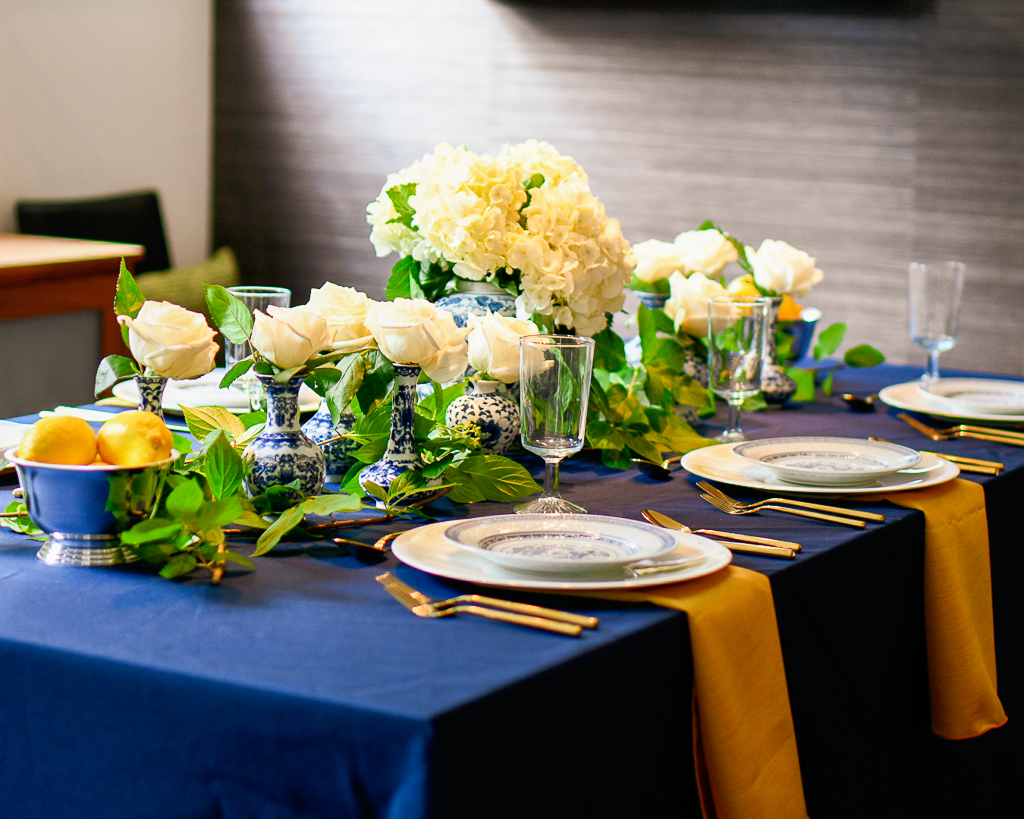 Blue tablecloth with chinoiserie accents, gold flatware and gold napkins, silver bowls with fresh lemons.