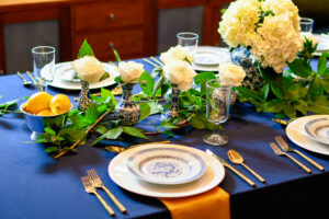 This beautiful blue table setting contains chinoiserie vases with ivory roses, as well as a chinoiserie ginger jar with white hydrangeas. Blue and white china is accented by gold flatware and gold napkins.