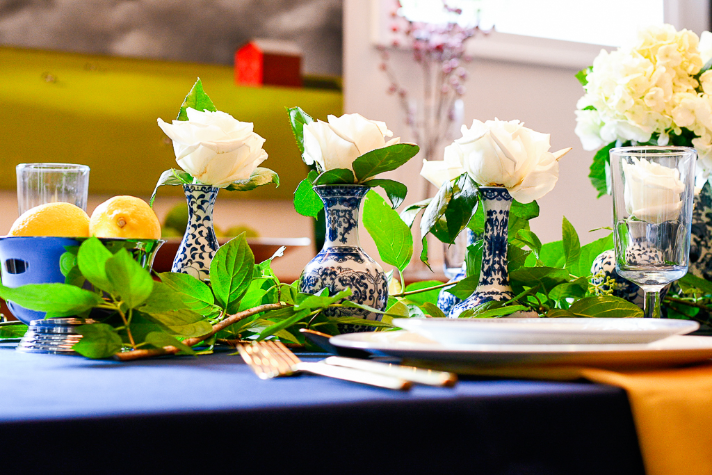 Chinoiserie bud vases with white roses down the center of a table with a navy tablecloth are a great blue table decorations idea.