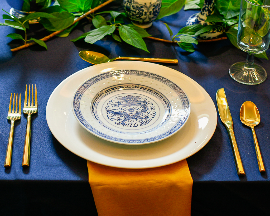 blue and white china, gold utensils, gold napkin, blue tablecloth, chinoiserie vase and white roses combine to illustrate how to use blue table decorations.