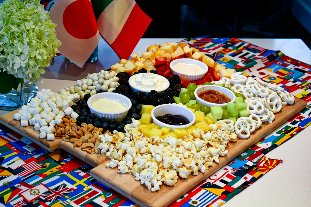 A charcuterie board with fruit arranged as the Olympic rings, assorted nuts, cake and fruit, as well as fruit dips. Olympic party ideas.