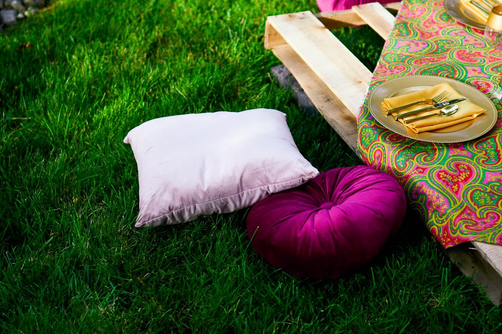 Pink velvet and magenta velvet cushions next to a wooden pallet that has been repurposed as a picnic table. Simple picnic ideas.