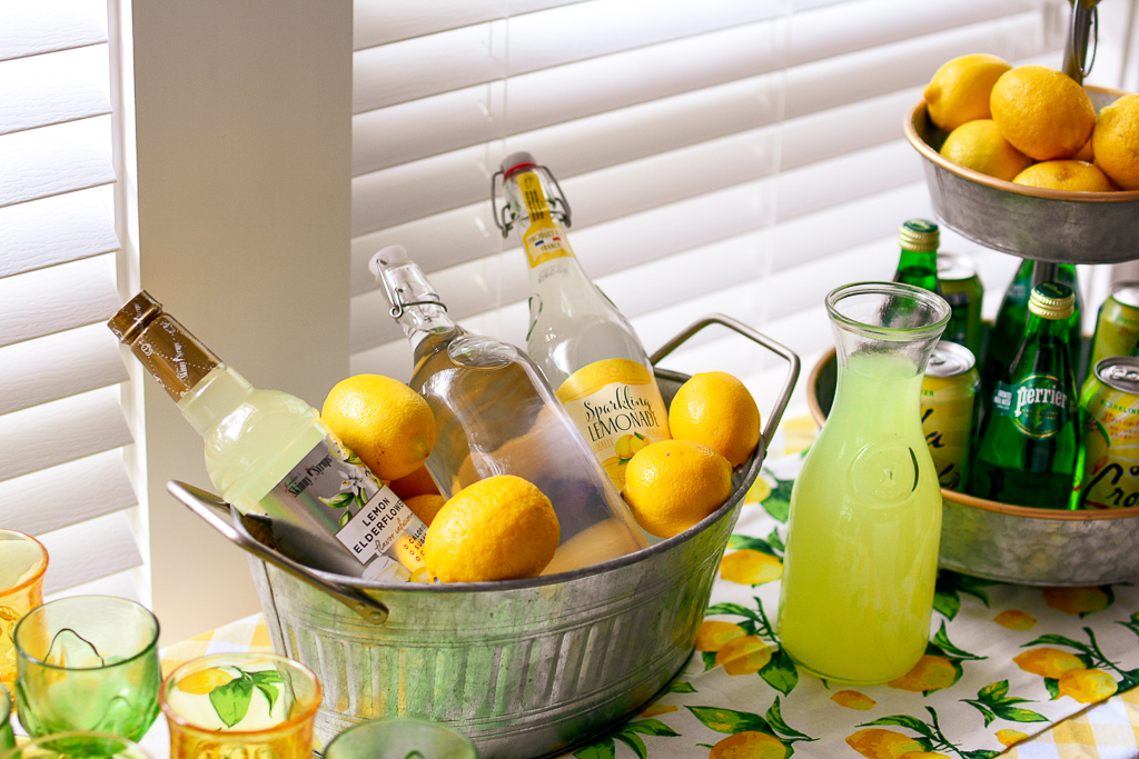 what is limoncello, the best limoncello recipe, limoncello cocktail, limoncello recipes, limoncello martini, summer party ideas, galvanized tub with lemons and lemon flavored liqueur, lemonade, galvanized tiered tray with lemons, lemon table runner, vintage yellow and green glasses, lemonade cocktails, best alcohol to mix with lemonade, lemonade cocktail with vodka